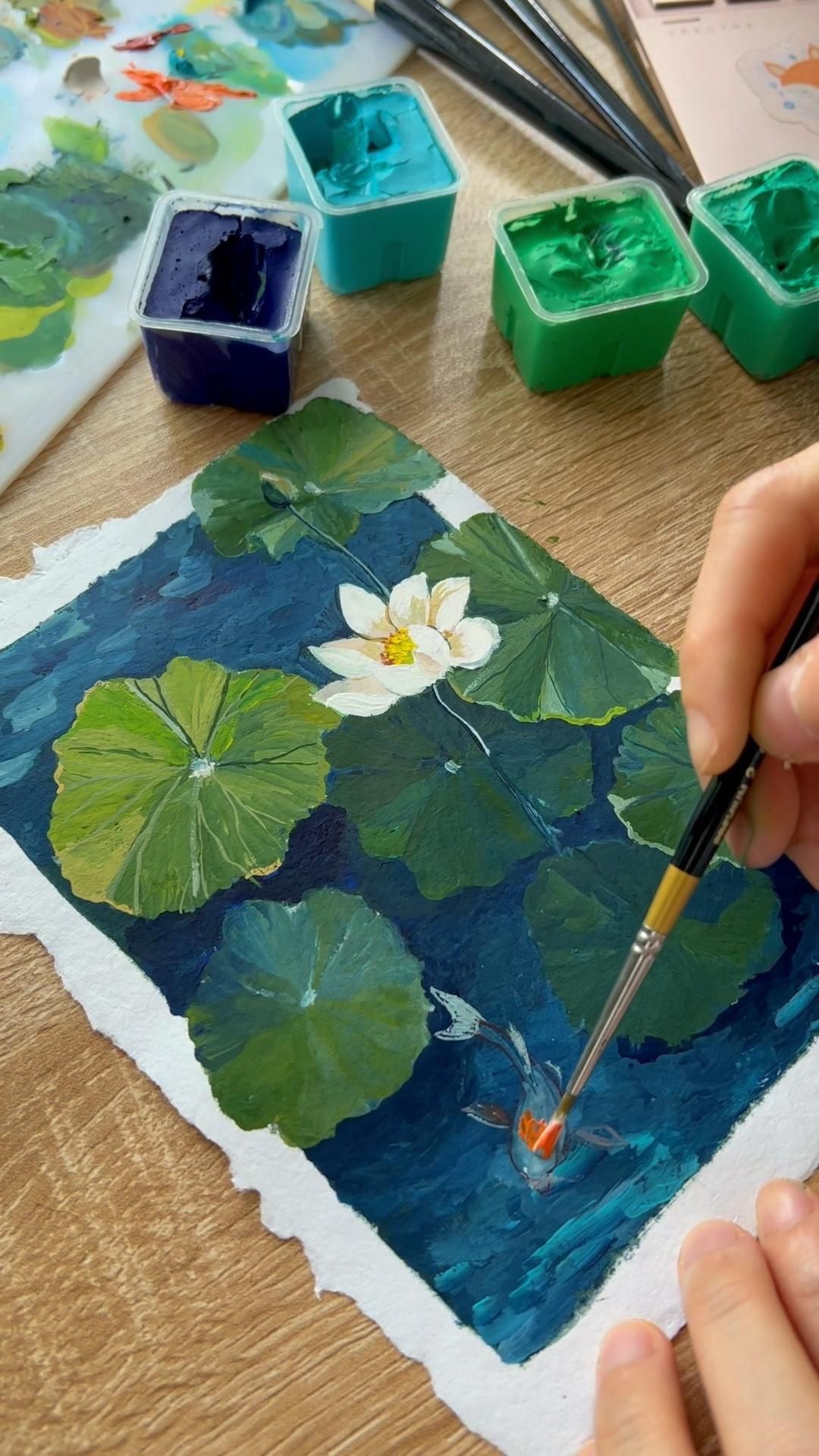 Đang tô màu gouache một con cá koi nhỏ dưới lá sen và một bông sen trắng