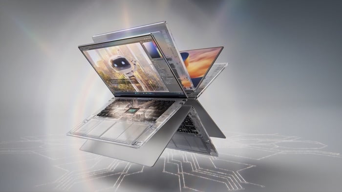 Hai chiếc laptop mỏng mở ra quay lưng vào nhau trên nền xám, màn hình hiển thị phần mềm chỉnh ảnh và dựng hình, bên dưới là mạch điện tử phát sáng