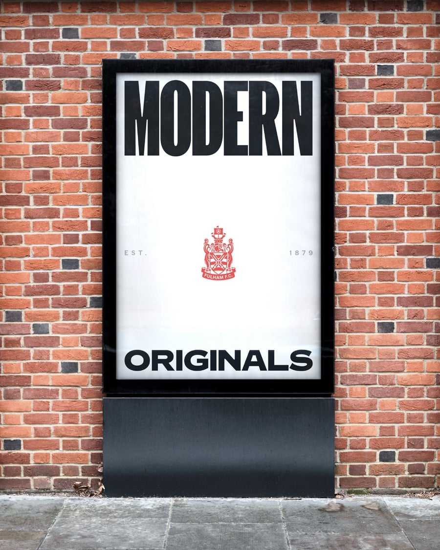 Biển quảng cáo đứng trên nền tường gạch đỏ, poster trắng có chữ MODERN ở trên, ORIGINALS ở dưới và biểu tượng đỏ ở giữa