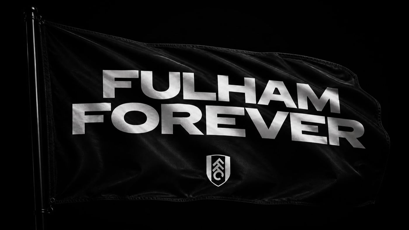 Lá cờ đen bay trong gió, in chữ FULHAM FOREVER màu bạc lớn và biểu tượng câu lạc bộ phía dưới