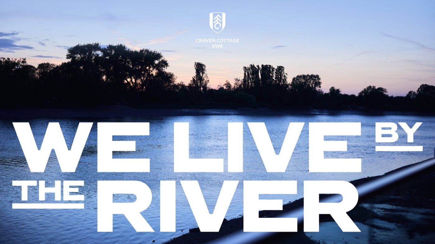 Ảnh bờ sông Thames lúc hoàng hôn, hàng cây đen in trên nền trời, dòng chữ trắng rất lớn WE LIVE BY THE RIVER đặt ngang qua mặt nước