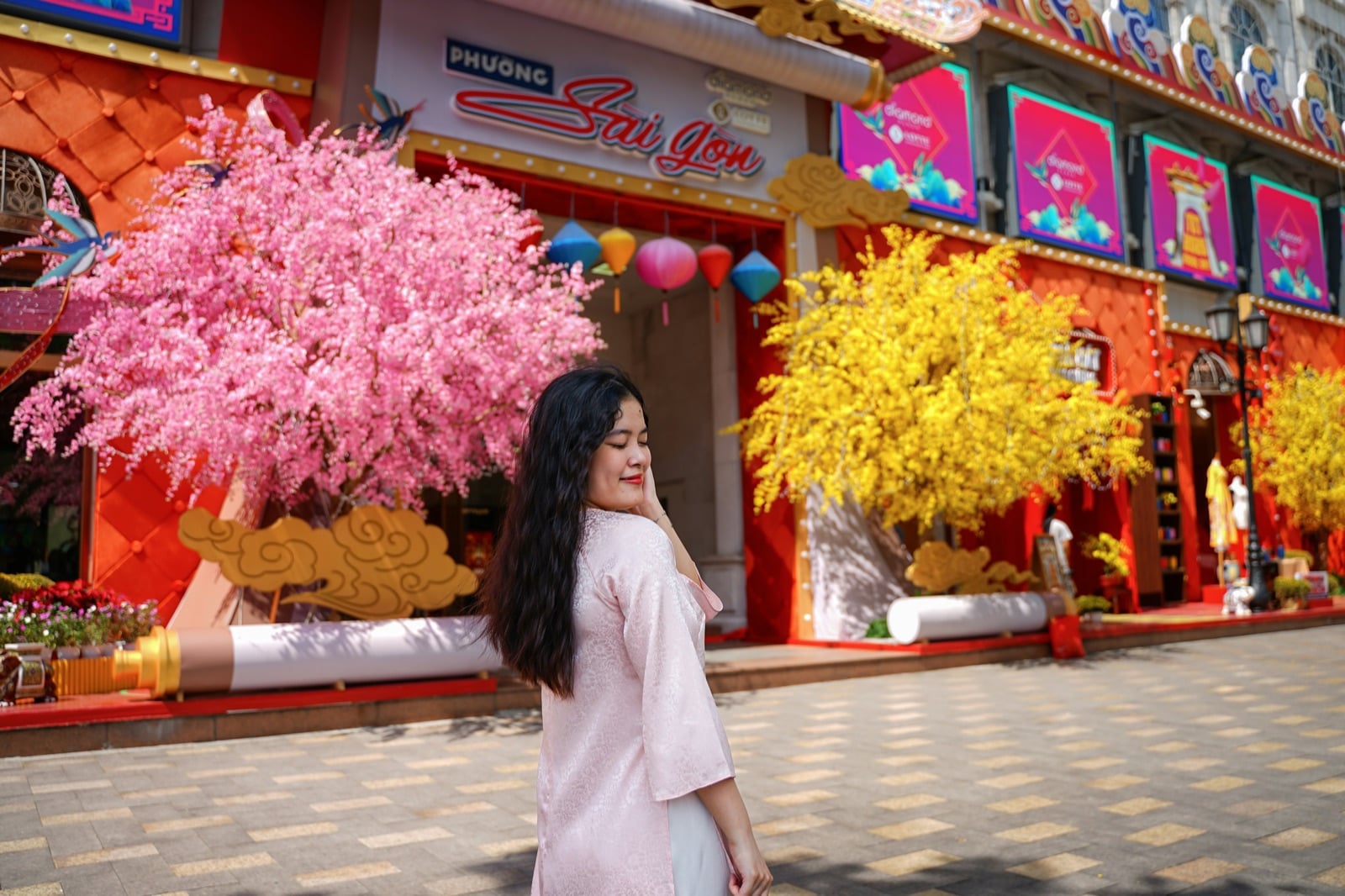 Cô gái mặc áo dài hồng phấn trước cây hoa đào và hoa mai trang trí Tết