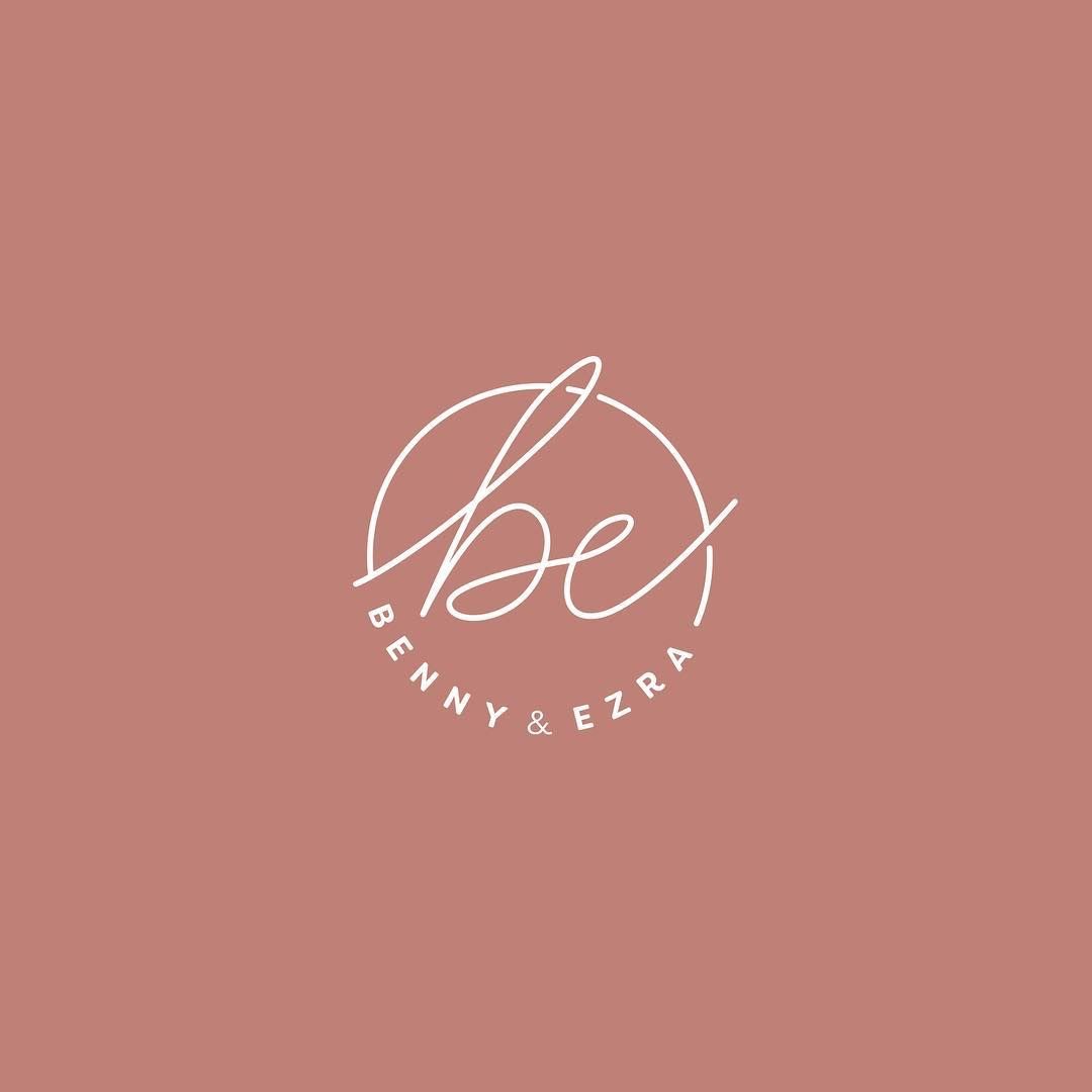 Logo tròn Benny & Ezra: chữ viết tay be cắt ngang vòng tròn hở, tên thương hiệu giãn rộng chạy vòng phía dưới, chữ trắng trên nền hồng đất