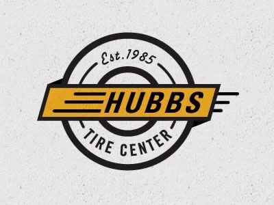 Logo Hubbs Tire Center: vòng lốp đen dày, dải vàng chéo có chữ HUBBS và các vạch tốc độ, chữ TIRE CENTER chạy theo vòng