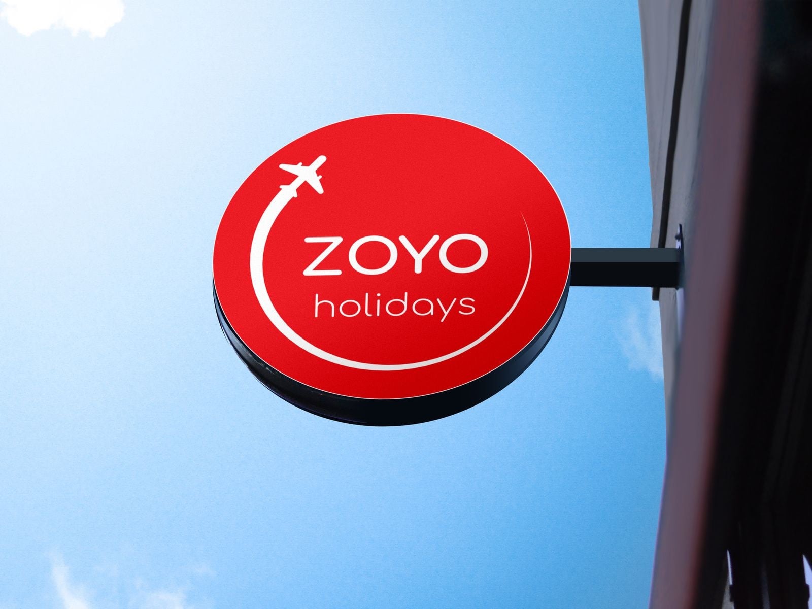 Logo Zoyo holidays trên biển treo tròn màu đỏ: máy bay trắng nhỏ kéo theo một đường bay cong ôm lấy chữ ZOYO