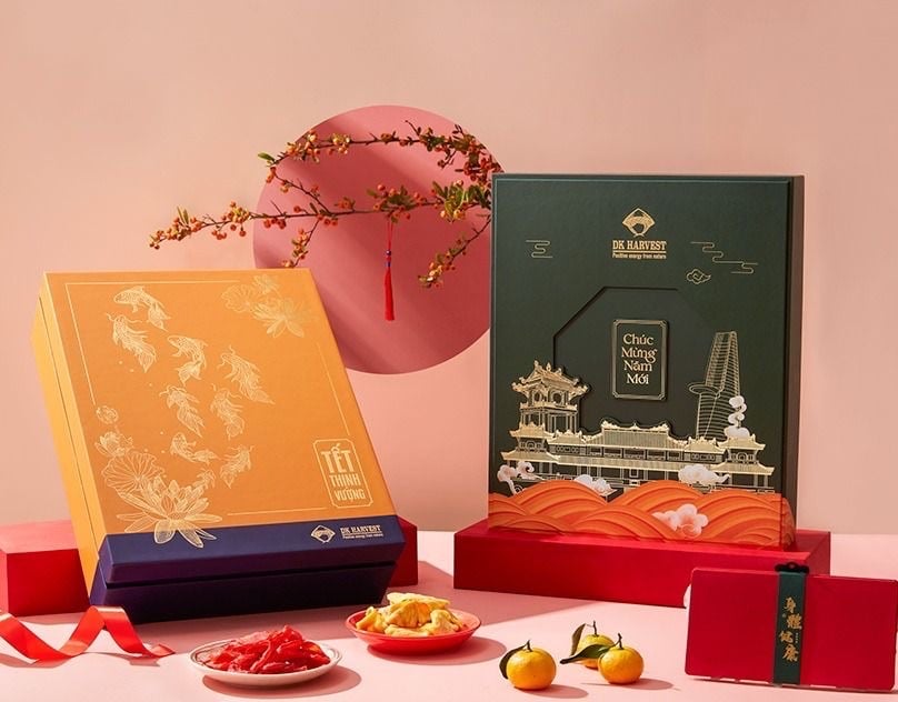 Hai hộp quà Tết, hộp cam có hoa sen và cá chép nét vàng, hộp xanh rêu có hình kiến trúc, sóng nước và chữ Chúc Mừng Năm Mới